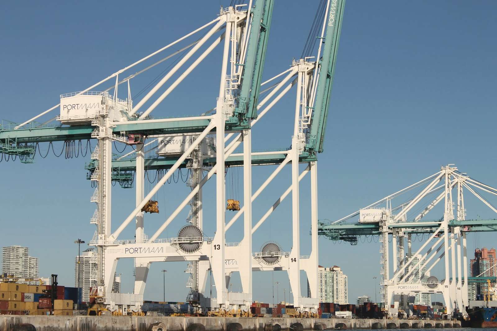 White and teal container cranes at PortMiami in daylight, with stacked containers on the quay
